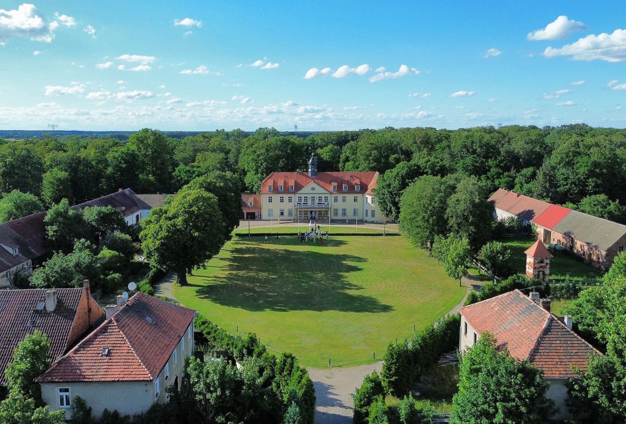 Luftaufnahme vom Schloss Grochwitz mit rotem Dach, großer Wiese, Nebengebäuden und dichtem Wald unter blauem Himmel., Foto: Bettina Unterkofler, Lizenz: Bettina Unterkofler