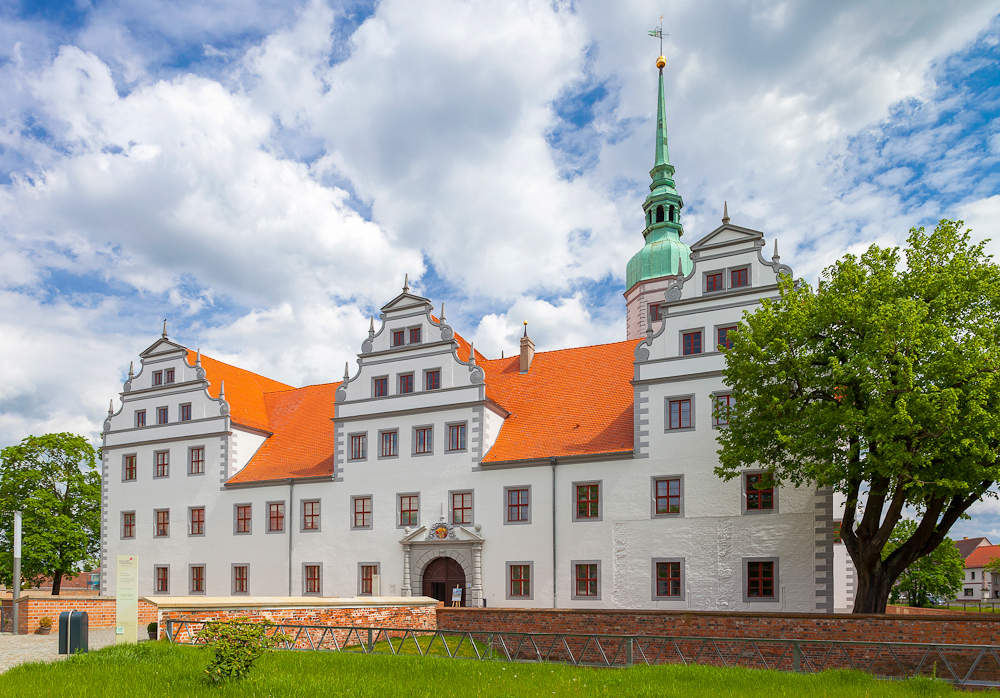 Weißes Schloss mit roten Ziegeldächern, Stufengiebeln und grünem Turm vor wolkigem Himmel; Baum im Vordergrund., Foto: Andreas Franke, Lizenz: Andreas Franke